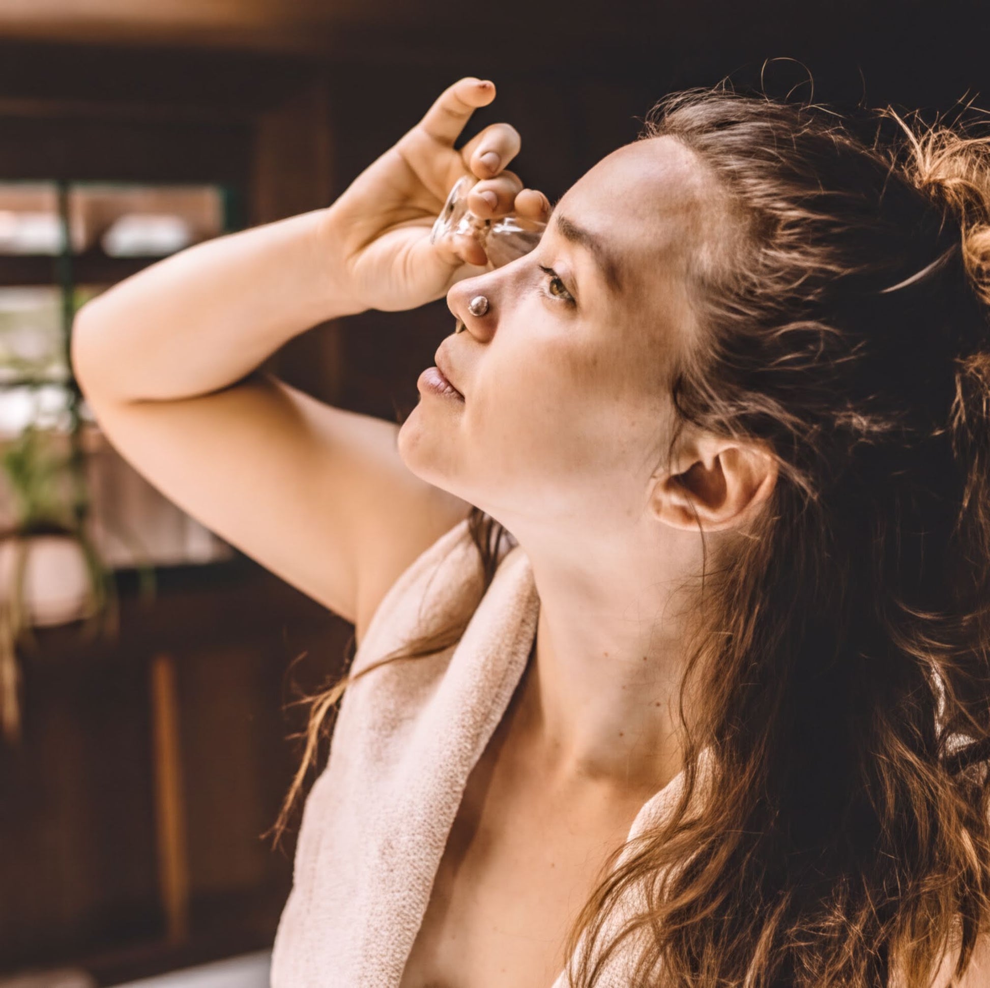 A woman with long brown hair is holding a small object to her eye, possibly cleaning her eye or applying makeup.