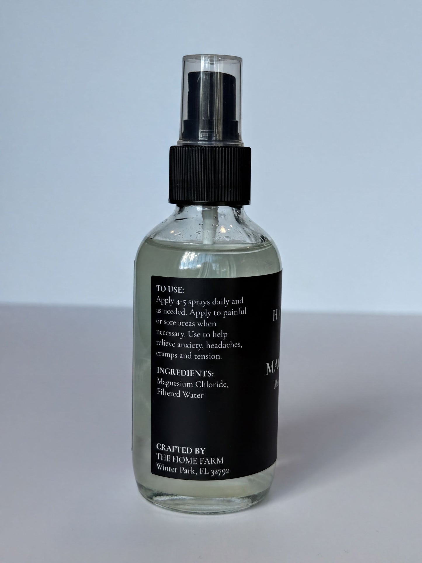 A clear glass bottle with a black cap, containing a clear liquid, and a black label with white text.