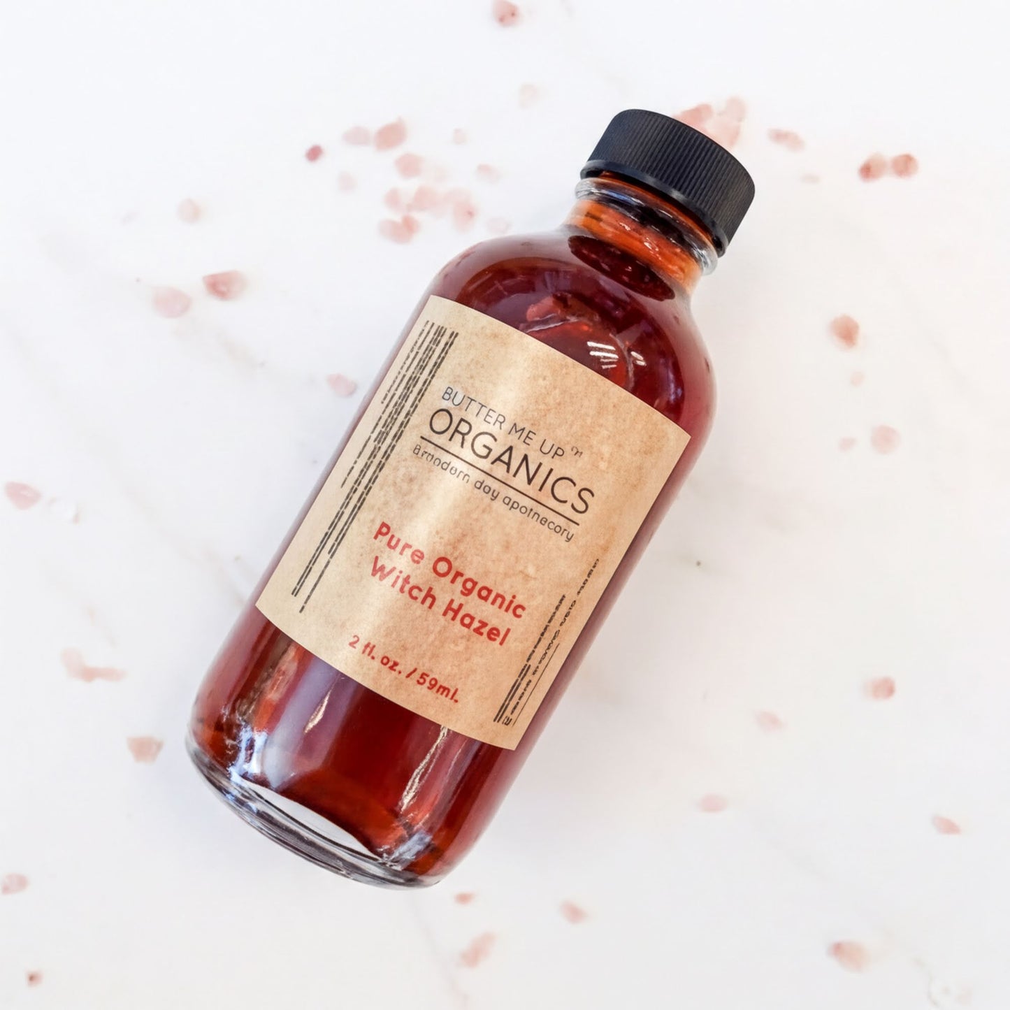 A bottle of pure organic witch hazel with a black cap, placed on a white surface with scattered red spots.