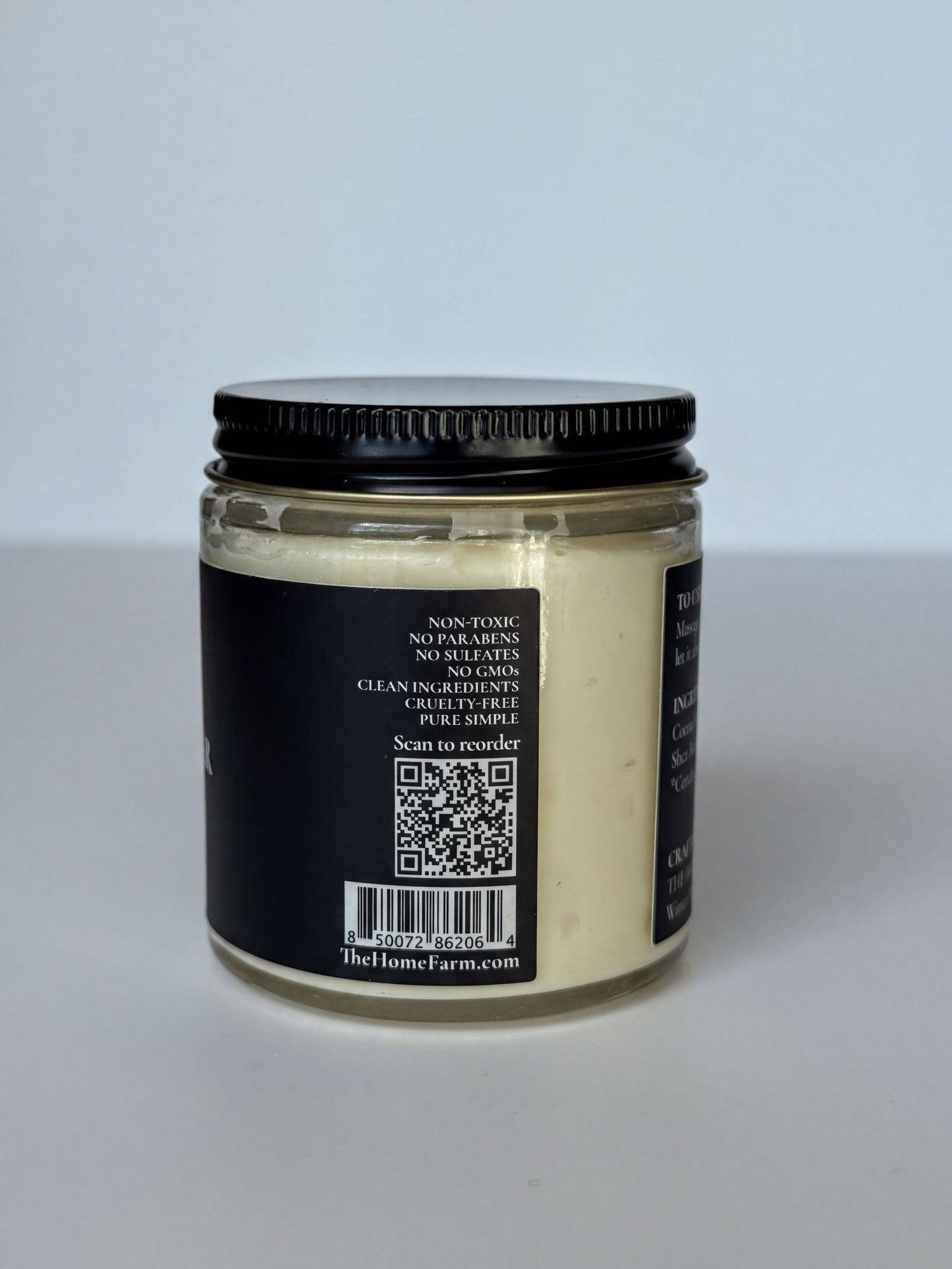 a jar of cream with a black lid, sitting on a white surface.