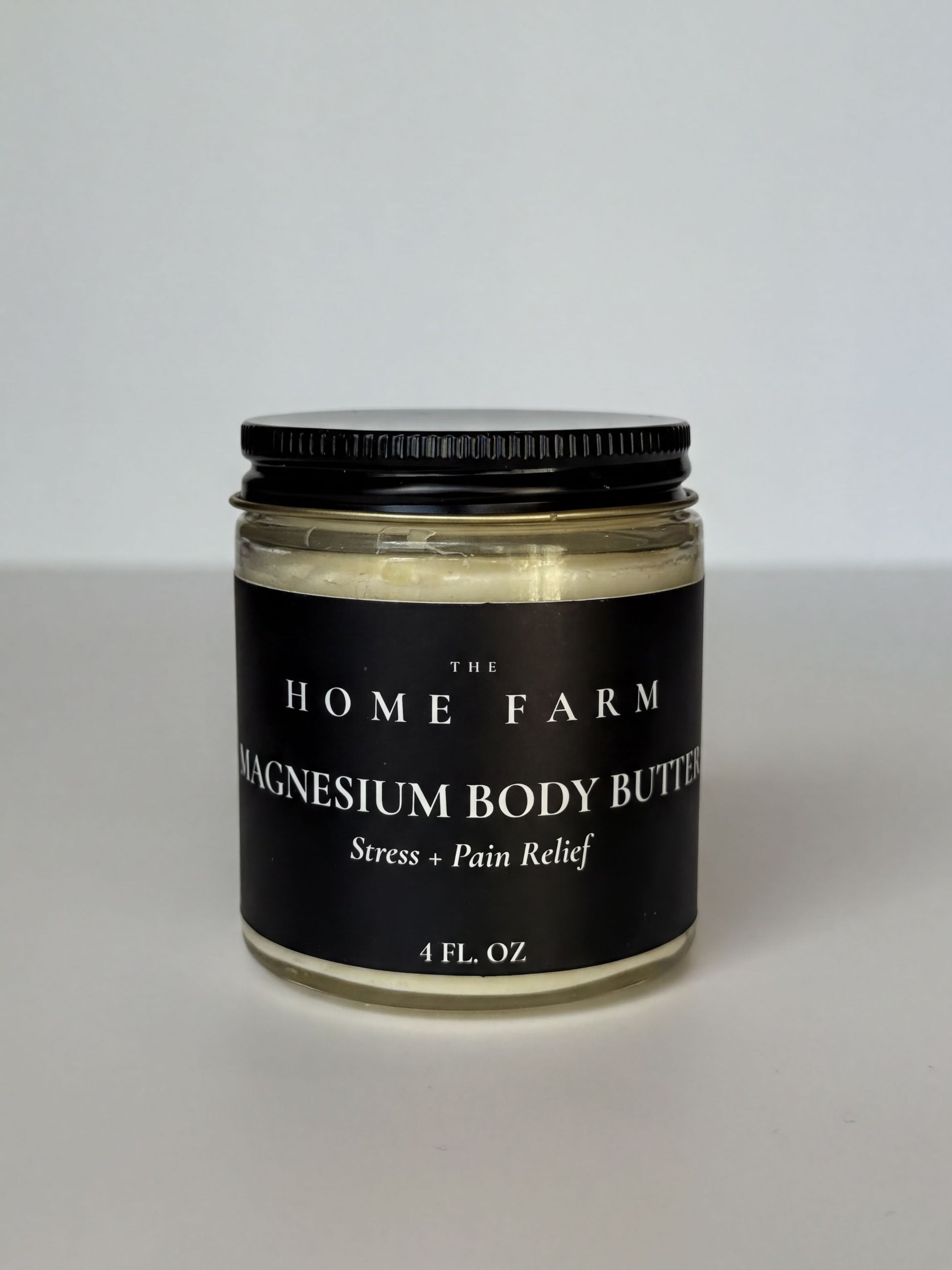 A jar of magnesium body butter with a black label that reads "The Home Farm" and "Magnesium Body Butter Stress + Pain Relief 4 FL. OZ."