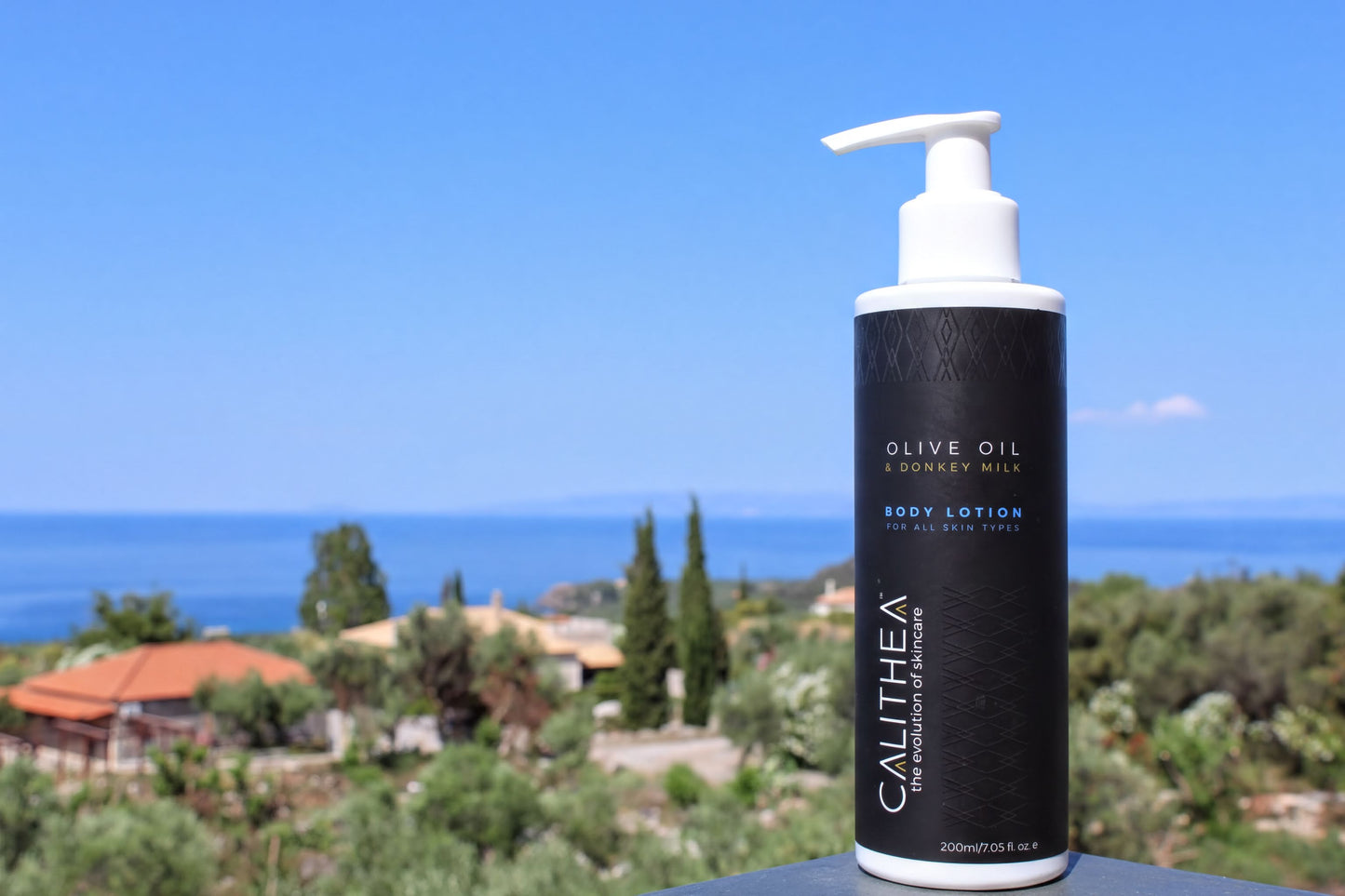 A pump bottle of body lotion with a clear blue sky and a body of water in the background.