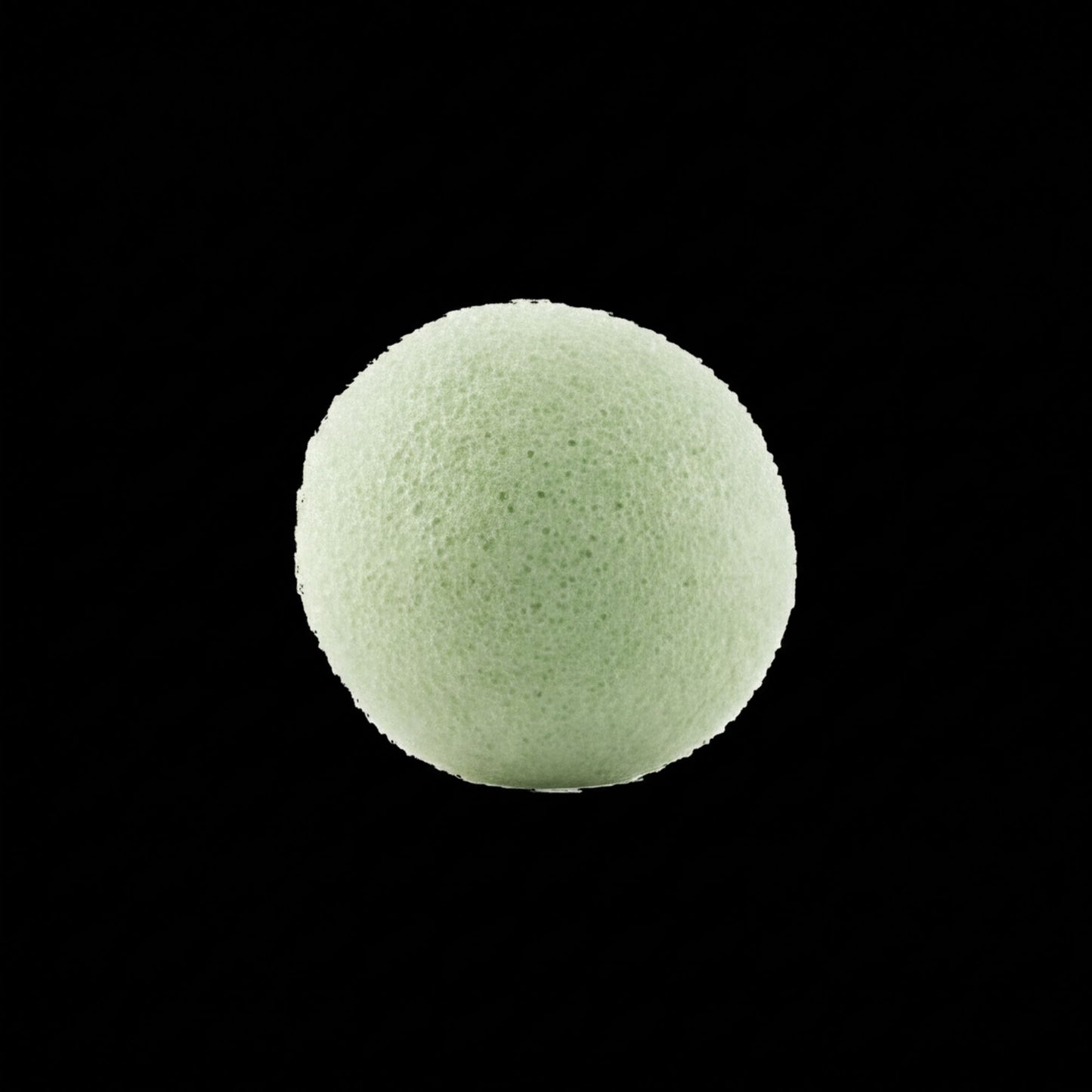 A single, round, green sponge against a black background.