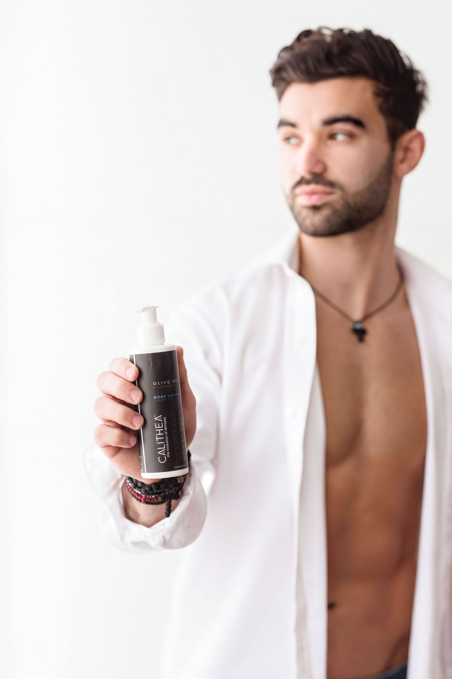 A shirtless man holding a bottle of olive oil in front of him.