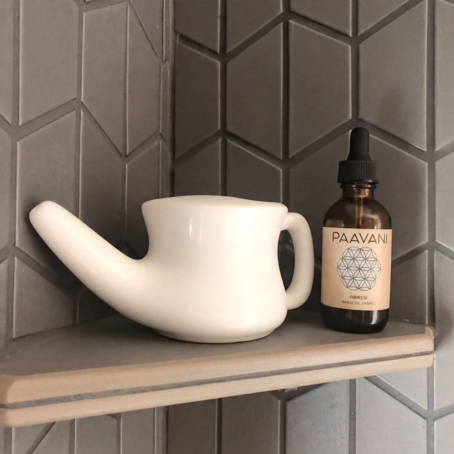 A white teapot and a brown bottle of PAAVAN essential oil are placed on a gray tiled shelf.