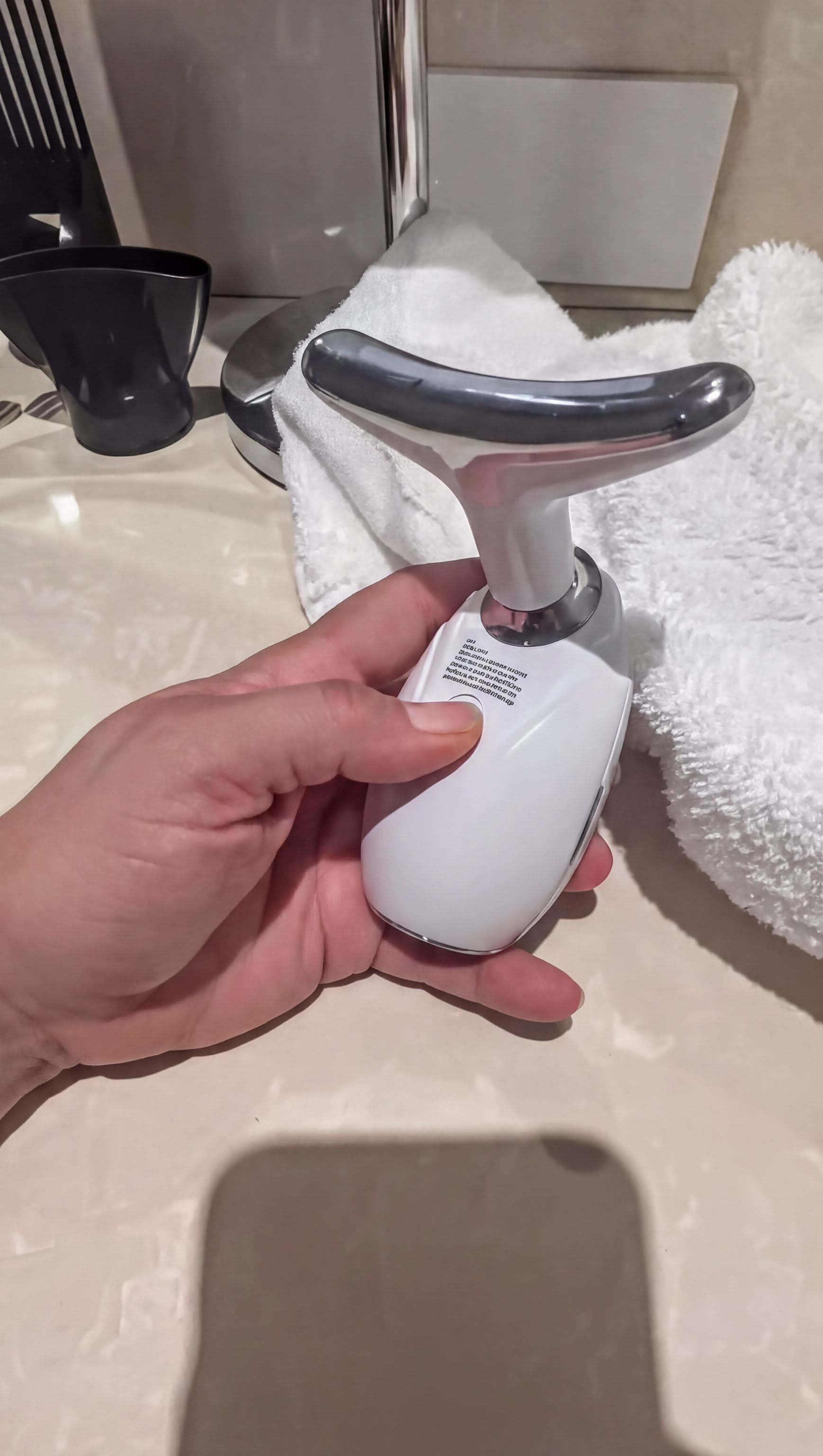 A person's hand is holding a white electronic device with a curved handle, which appears to be a device used for stretching or exercising.