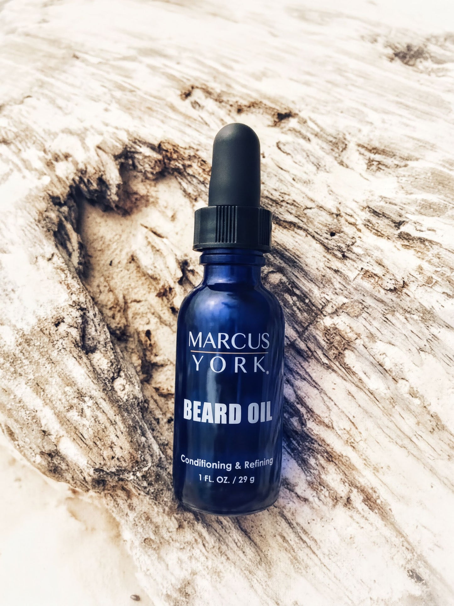 A blue bottle of Marcus York Beard Oil is placed on a textured surface, with a natural, wood-like background.