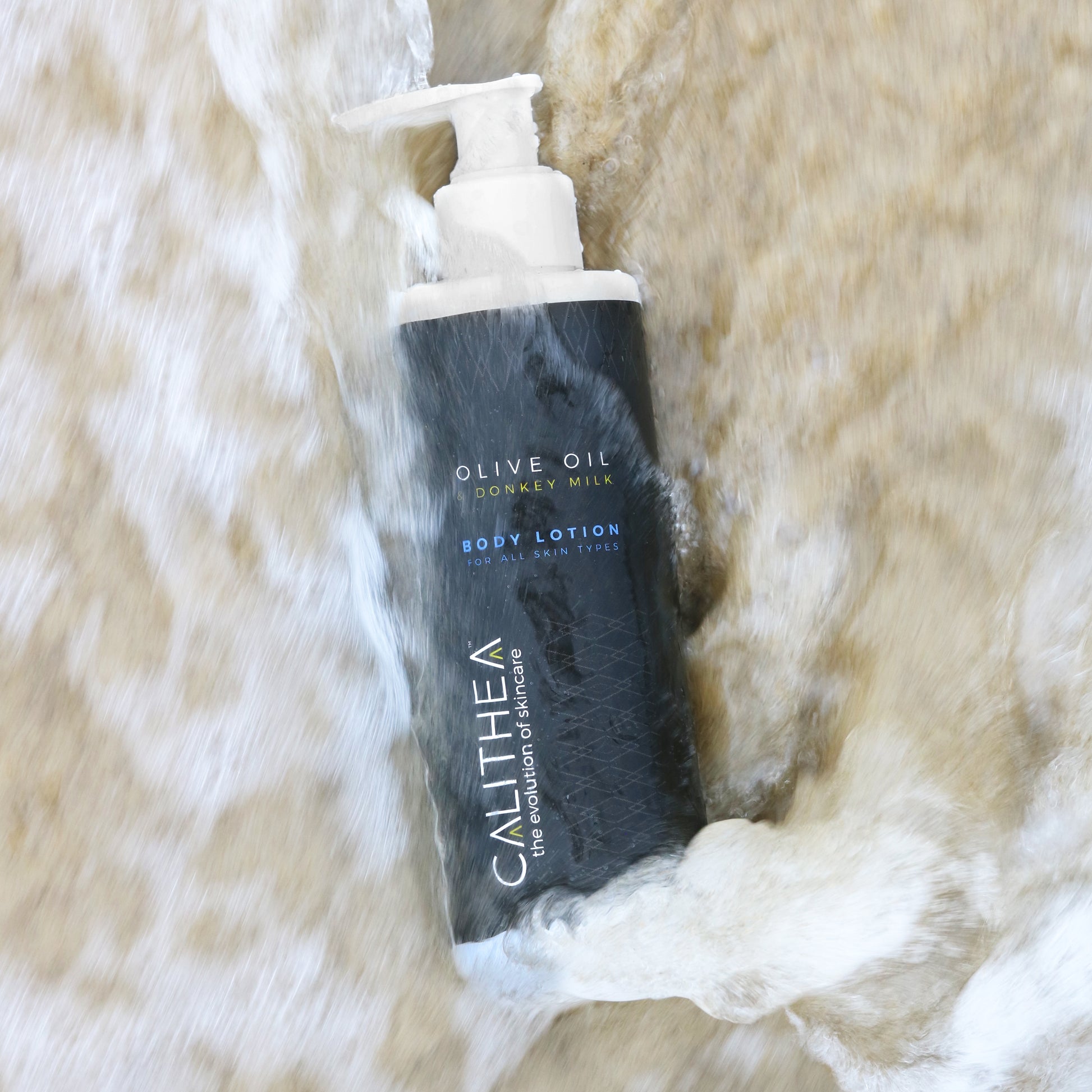 A bottle of body lotion with a pump dispenser, placed on a surface with water splashing around it.