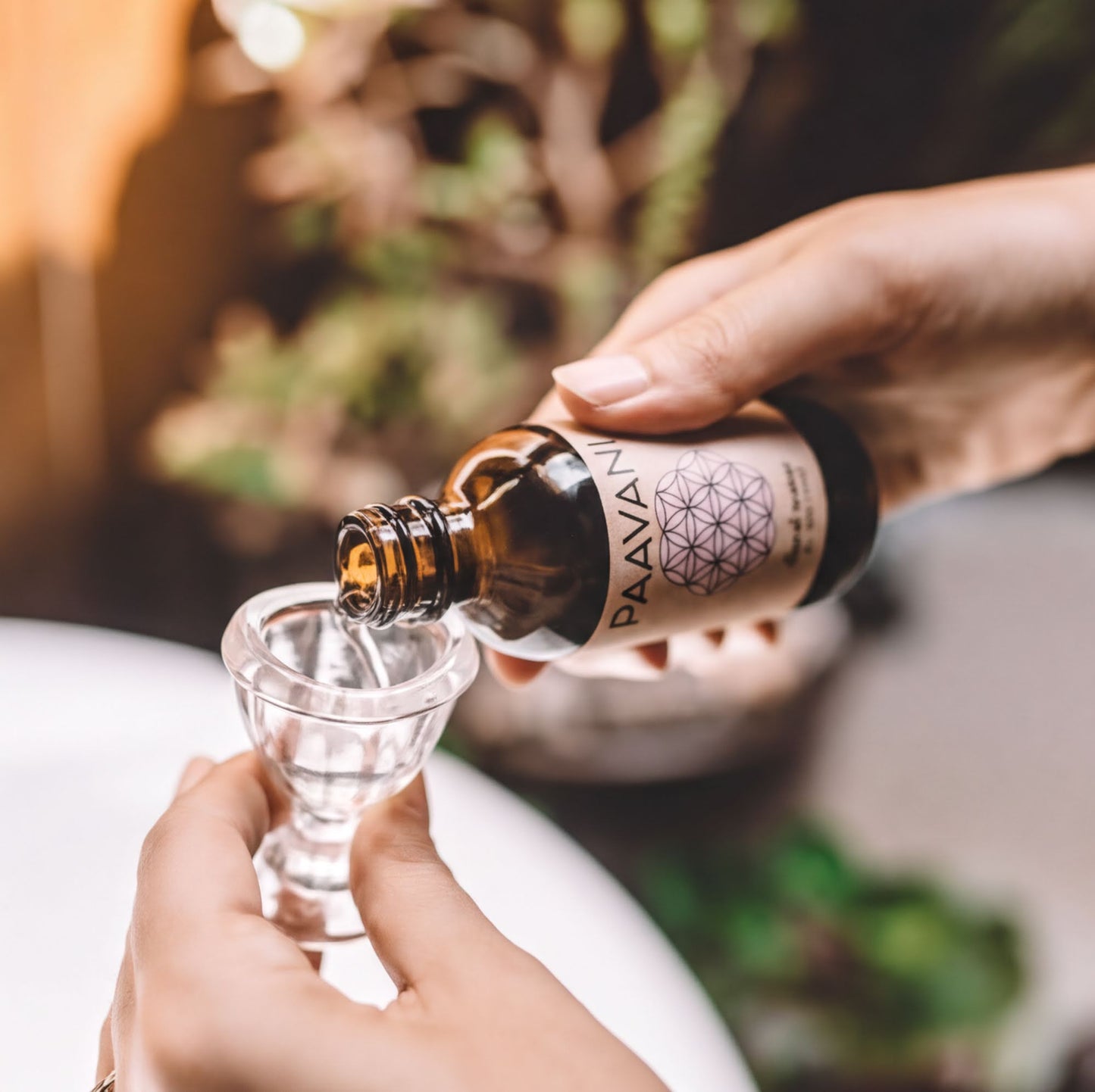 A person's hand is pouring a liquid from a brown bottle into a small glass container.